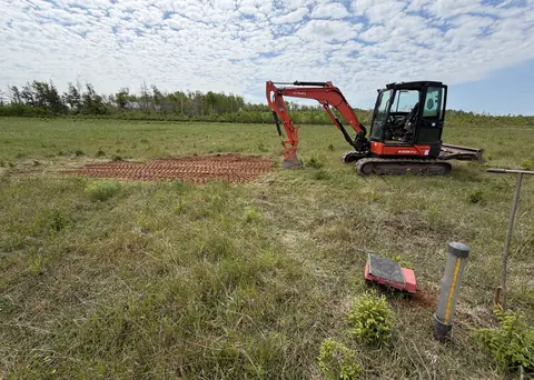 Mini excavator parked beside a prepared stone bed in a grassy field