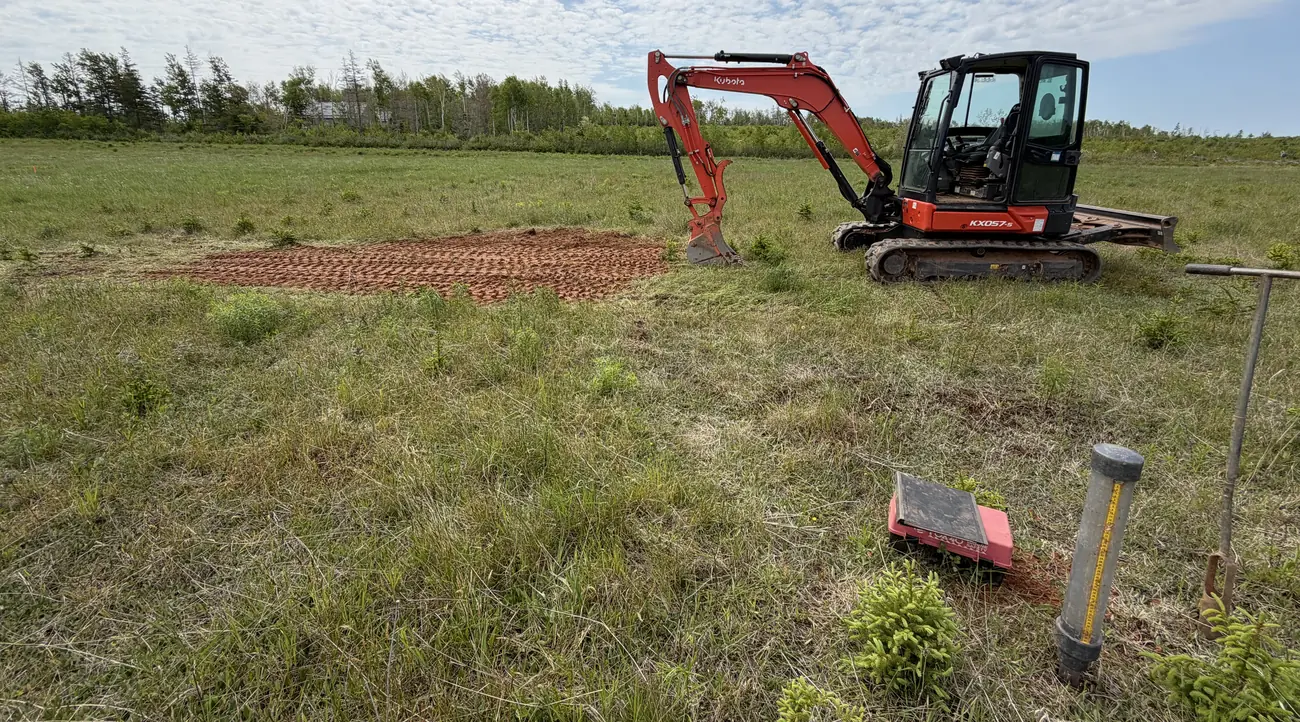 Mini excavator in a grassy field beside a prepared stone bed