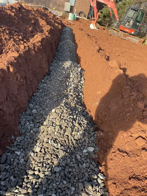 Stone-filled trench with an excavator at the far end